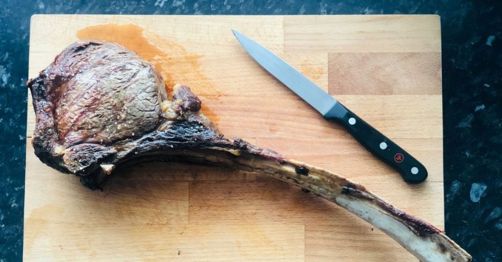 Sharp boning knife on a cutting board with a large piece of meat, used for trimming meat from the bone.