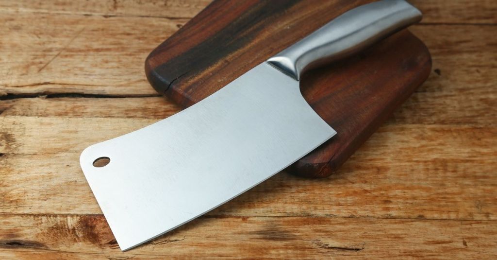 Large stainless steel butcher knife on a wooden cutting board, designed for tough cuts of meat.