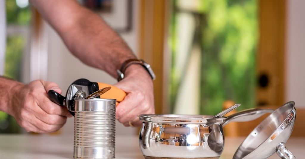 Person using a can opener to open a tin can, a practical kitchen tool.