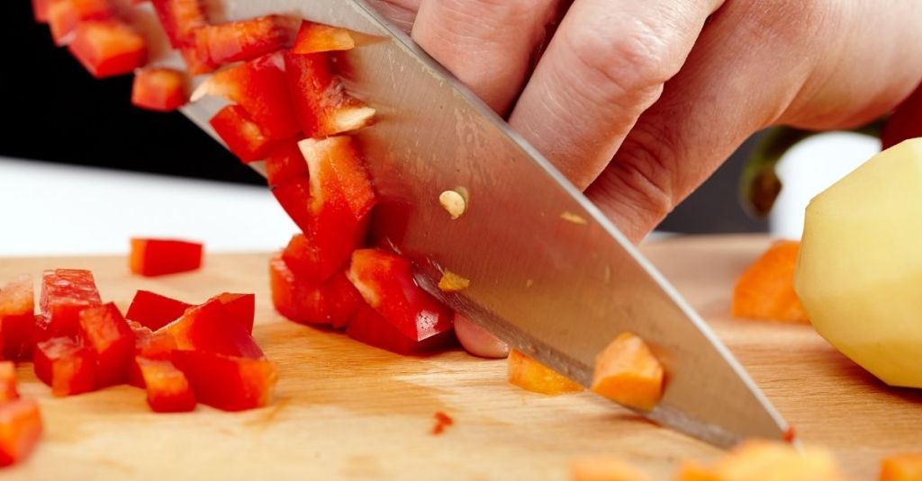 Chef knife cutting through red pepper on a wooden board, ideal for chopping and slicing.