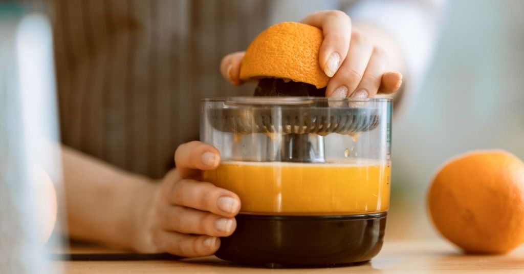 Person using a handheld citrus juicer to extract juice from an orange.
