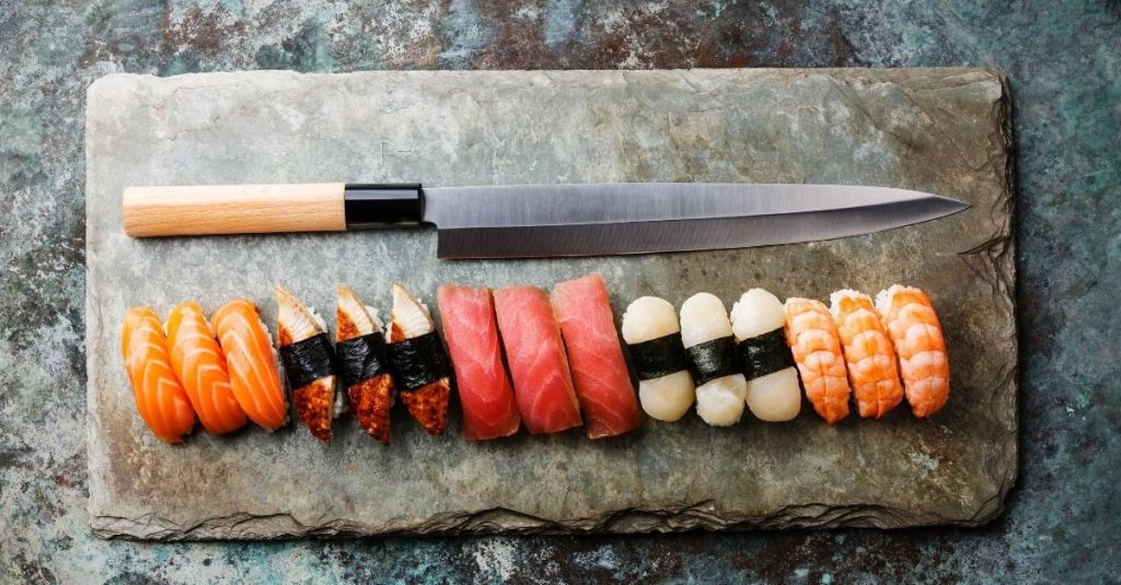 Sharp fillet knife on a stone plate with assorted sushi, ideal for delicate slicing.
