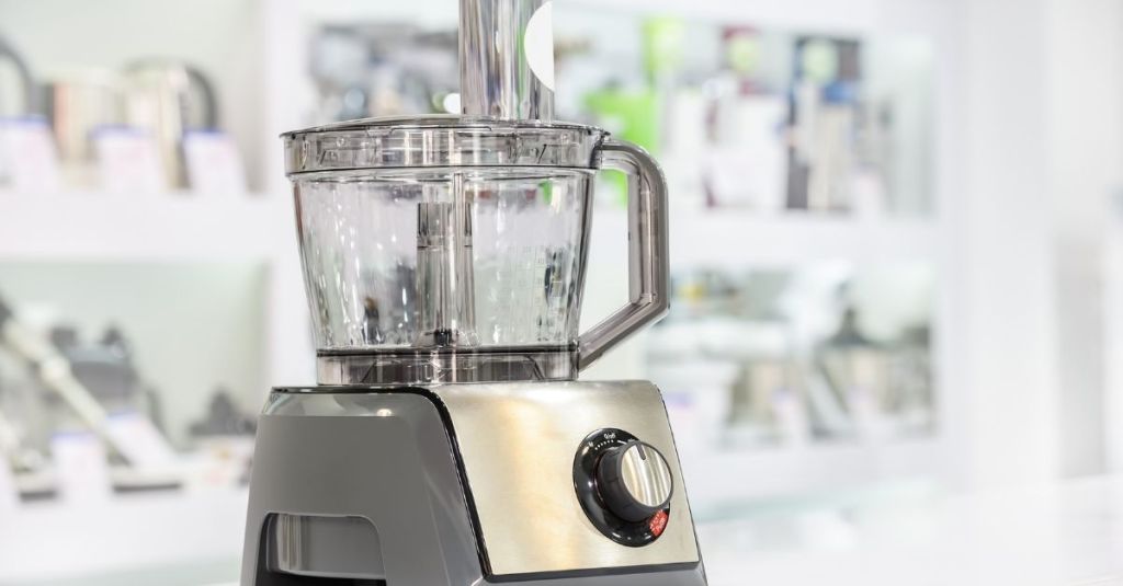Stainless steel food processor with clear bowl and control knob, suitable for slicing, dicing, and mixing various ingredients.