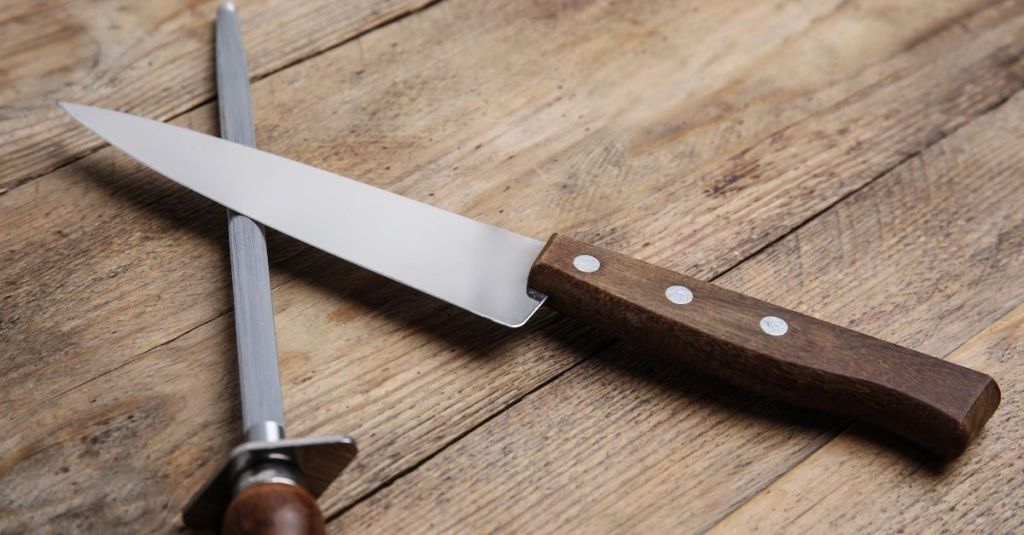 Honing steel and knife on a wooden surface, ideal for sharpening kitchen knives
