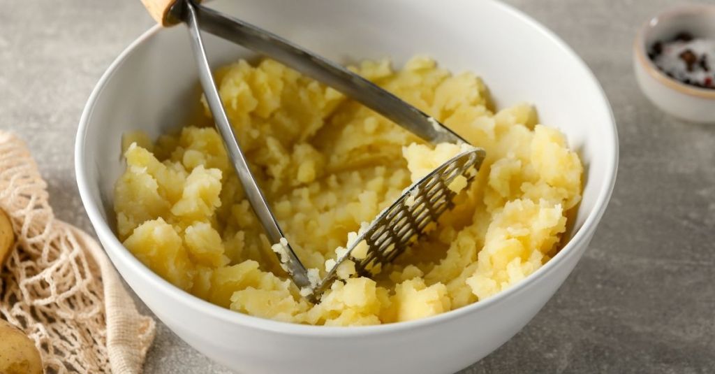 Potato masher pressing down in a bowl of mashed potatoes