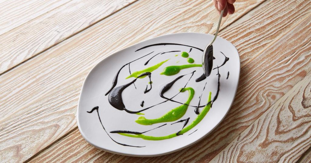 A white plate decorated with black and green gels in artistic swirls, showcasing modern culinary plating techniques.