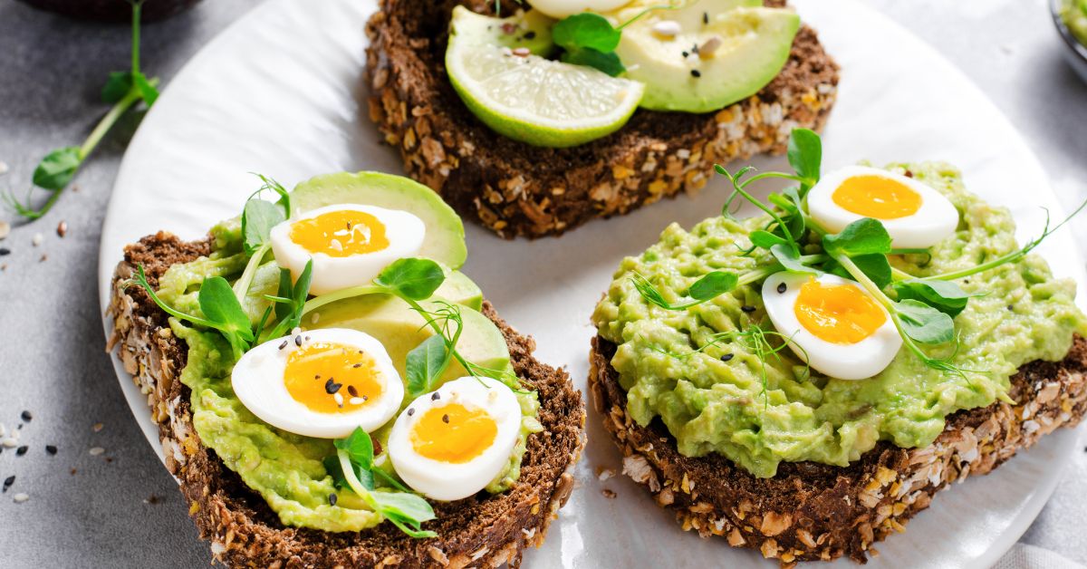 Avocado toast with eggs provides a rich source of healthy fats and protein. Avocado toast garnished with soft-boiled eggs and microgreens, showcasing a healthy and colorful plant-based meal.