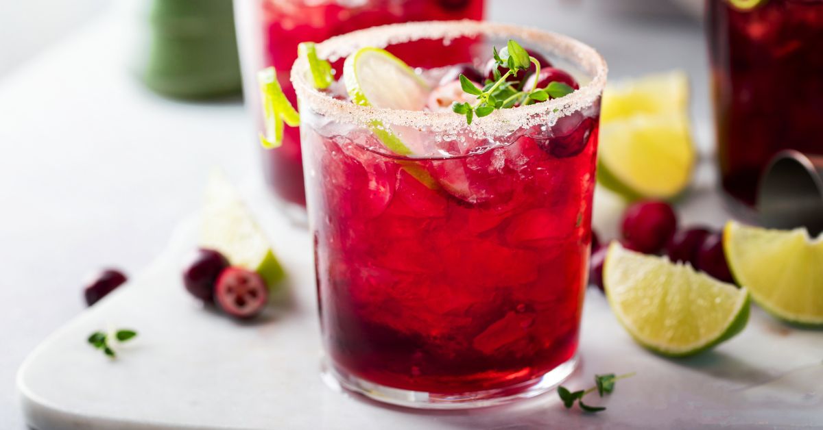 Non-alcoholic cranberry mocktail with lime and a salted rim, garnished with herbs.