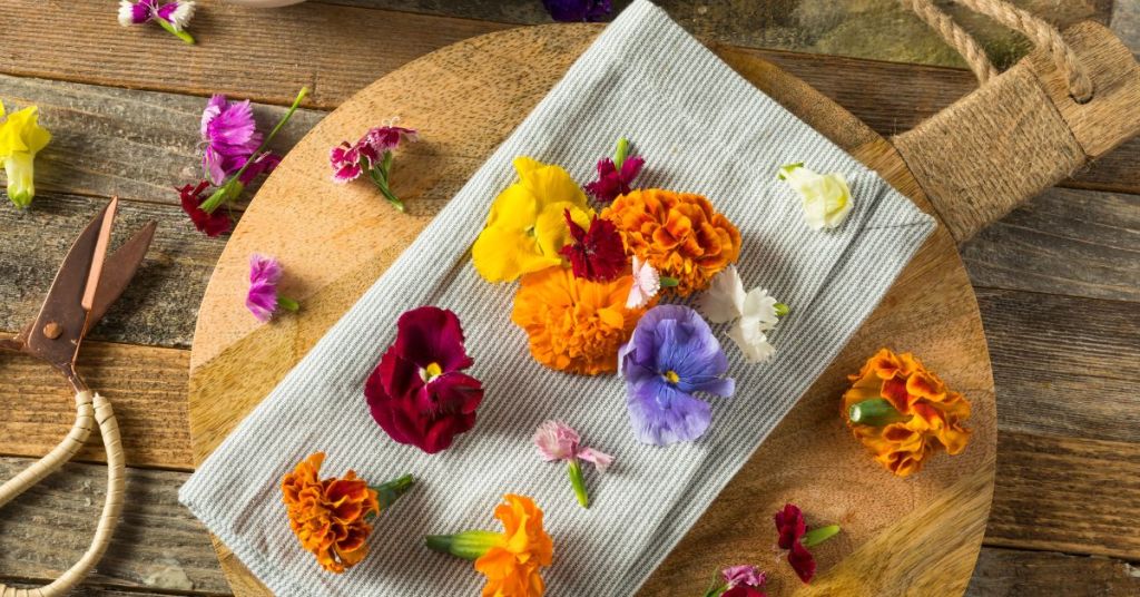 A variety of edible flowers, including marigolds and pansies, beautifully arranged on a wooden board for culinary use.