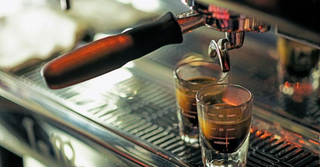 Espresso shot being pulled from a machine into glass cups.
