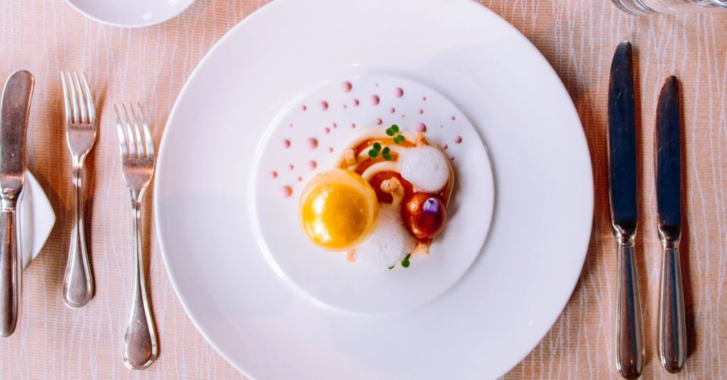 A gourmet dessert plated with golden gel spheres, foam, and delicate garnishes, showcasing advanced culinary techniques.