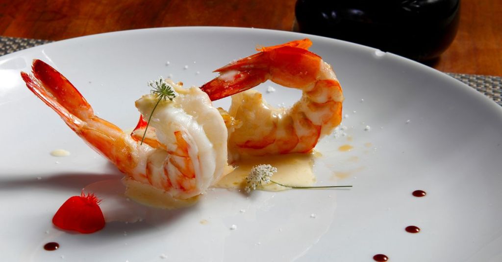 A gourmet shrimp dish served with a delicate sauce and floral garnish on a white plate, emphasizing elegance in plating.
