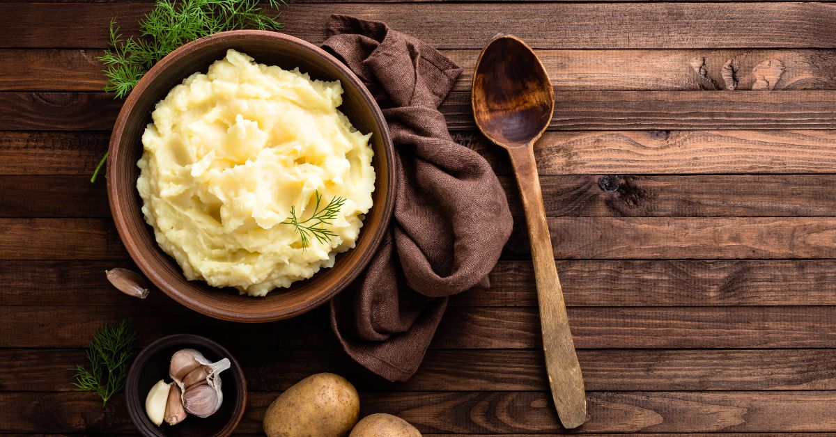 Creamy garlic mashed potatoes served in a wooden bowl, garnished with herbs, perfect for a plant-based Thanksgiving feast.