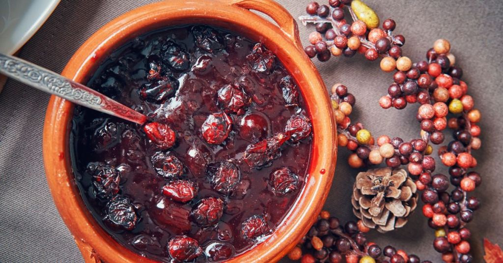 Homemade cranberry sauce with whole cranberries simmering in a clay pot, ideal for enhancing a plant-based Thanksgiving meal.