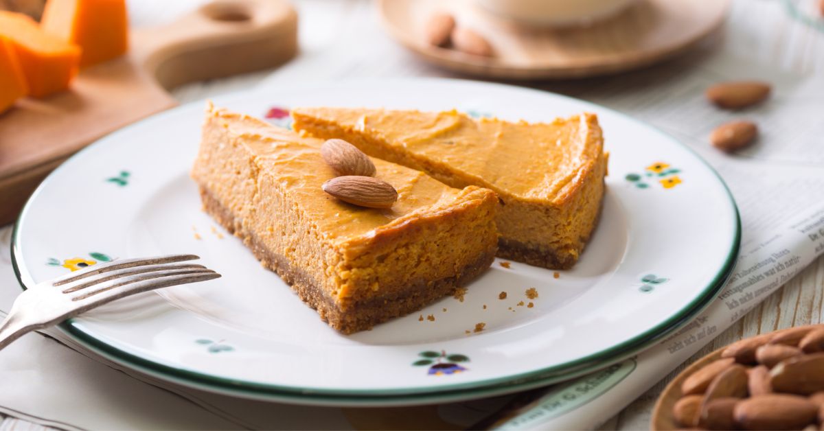 A slice of creamy pumpkin spice cheesecake topped with almonds, served on a floral plate, perfect for a plant-based dessert.