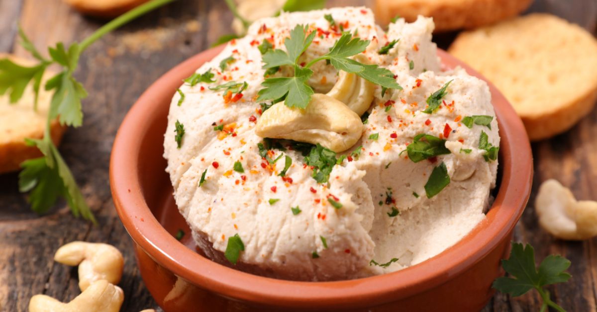 Cashew-based vegan cheese dip offers a tasty alternative for plant-based diets. A bowl of vegan cheese dip made from cashews, garnished with herbs and served with crackers, showcasing a flavorful plant-based appetizer.