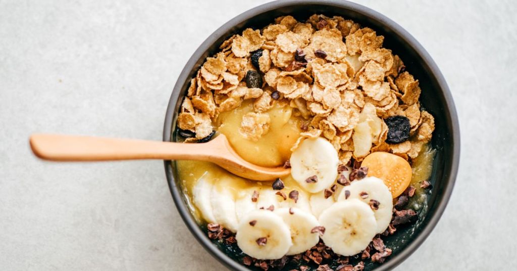 A bowl of cereal topped with banana slices and cacao nibs, ideal for an energy boosting breakfast. A black bowl filled with whole-grain cereal, fresh banana slices, cacao nibs, and a drizzle of natural honey, highlighting a nutritious breakfast option.