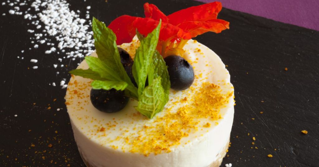 Cheesecake plated with blueberries, edible flowers, and mint leaves.