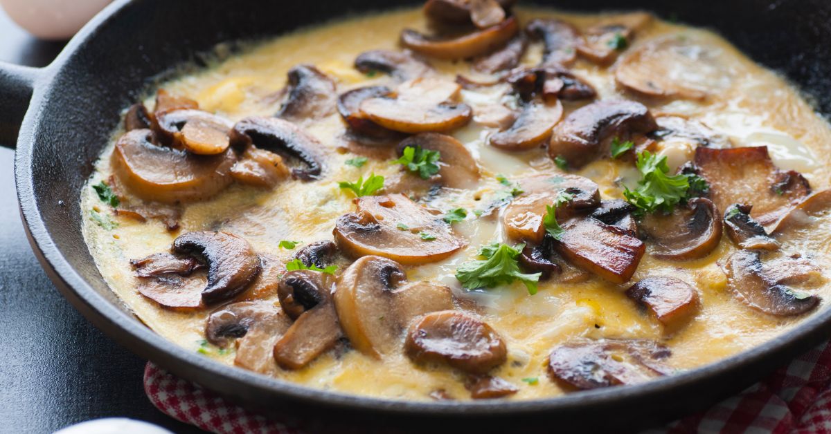 A creamy egg preparation filled with sautéed mushrooms and fresh parsley, served in a skillet.