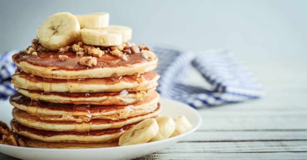 Stack of protein-packed pancakes topped with banana slices and walnuts, a delicious energy boosting breakfast option. A stack of banana pancakes drizzled with syrup and topped with walnuts, a perfect quick breakfast idea.