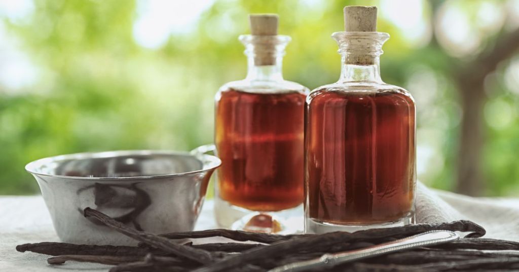 Glass bottles of homemade vanilla extract. Two glass bottles filled with homemade vanilla extract on a table with vanilla pods and tools nearby.