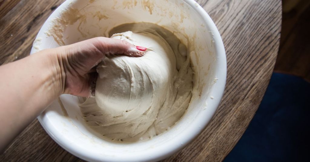 A hand kneading sourdough dough in a white bowl, showing the texture and elasticity of well-fermented dough.