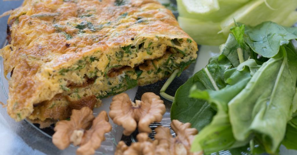A cross-section of Persian kuku sabzi, brimming with fresh herbs and walnuts, served with greens on the side.
