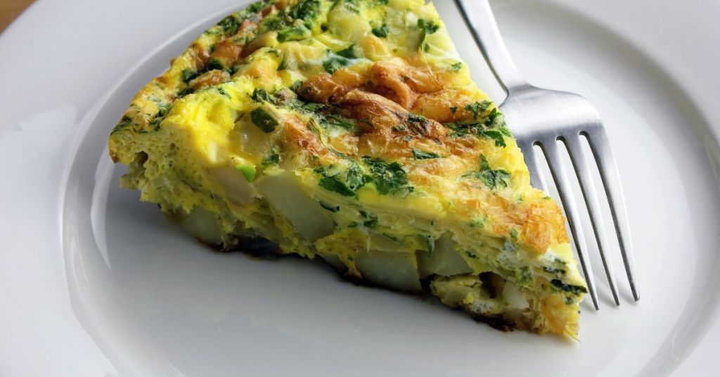 A slice of spinach and potato egg bake with golden edges and vibrant greens, served on a white plate.