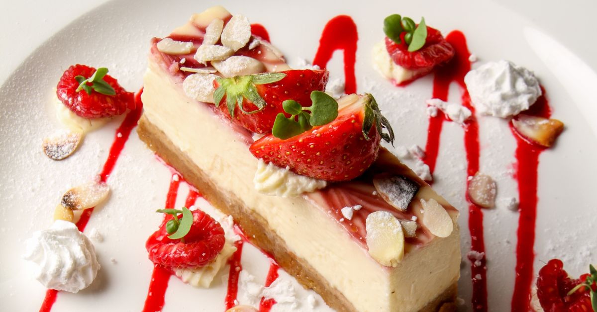 Plated strawberry cheesecake with vibrant raspberry sauce and garnished with almond slices.