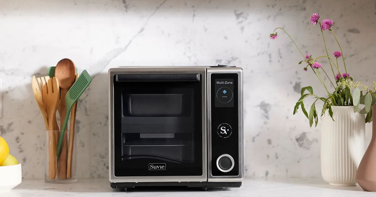 Smart kitchen robot with multi-zone cooking technology. Suvie Kitchen Robot on a marble countertop, surrounded by kitchen tools and flowers, offering advanced cooking technology.