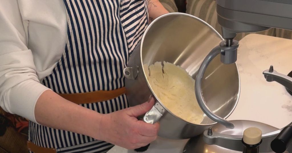 Person adding the bowl to a KitchenAid stand mixer with pre-measured ingredients nearby, ready to mix pasta dough.