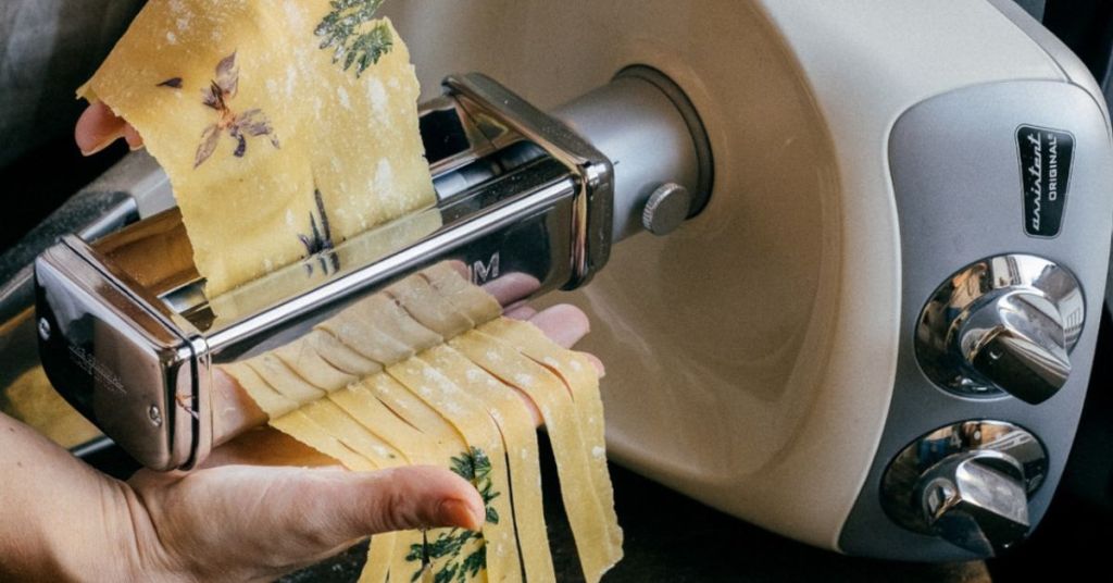 Ankarsrum mixer with pasta attachment in use, creating fresh pasta ribbons.