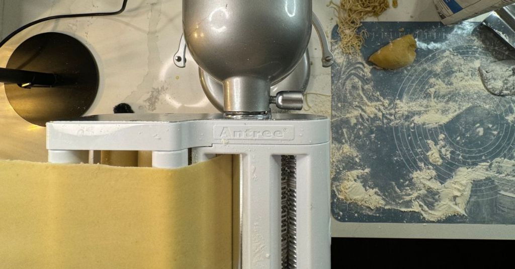 KitchenAid stand mixer with a pasta roller attachment, smoothing fresh dough into even sheets for homemade pasta.