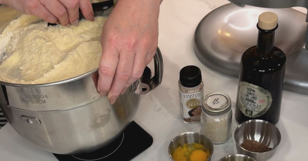 Hands using a fine sieve to sift flour onto a wooden surface, ensuring a lump-free base for pasta dough.
